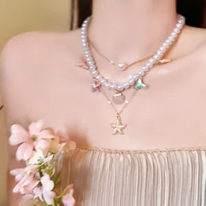 Detail view of a multi-layer pearl necklace featuring golden starfish and teal fishtail charms.