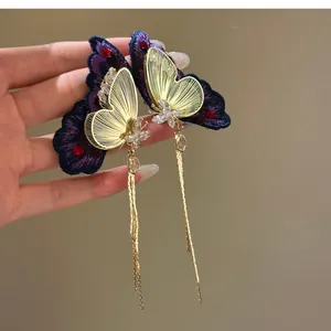 Detail shot of purple embroidered butterfly earrings with long golden chain tassels and crystals.