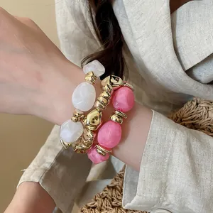 Primo piano di tre braccialetti elastici in acrilico irregolare rosa, bianco e oro.