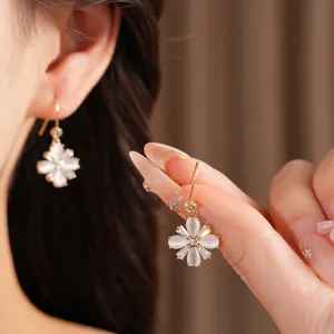 Detailansicht der eleganten Zirkon- und Katzenaugenstein-Blumenohrringe an einer Hand.