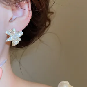 Primo piano di eleganti orecchini a lobo a fiore con perla e zirconi brillanti sull'orecchio.
