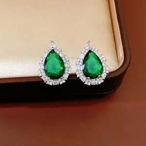 Detail shot of teardrop emerald green stud earrings with zircon halo in a luxury jewelry box