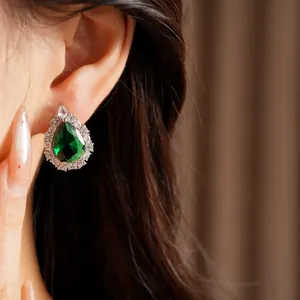 Detailed view of an elegant teardrop earring with emerald green zircon on model's ear