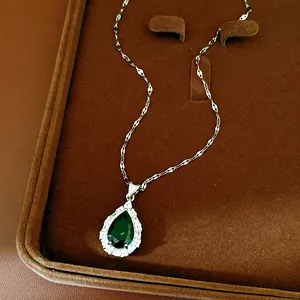 Close-up detail of a silver necklace with a brilliant teardrop green gemstone pendant