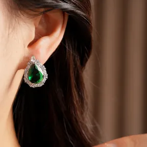 Detailed view of an elegant teardrop earring with green zircon worn on a model ear