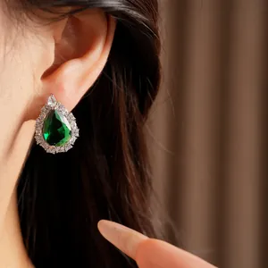 Close-up detail of luxury teardrop emerald green earring with sparkling zircon halo on ear