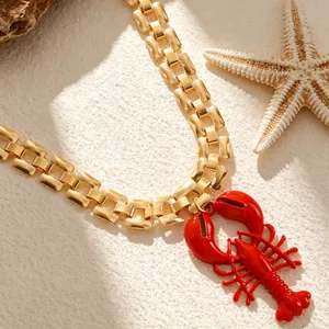 Close-up detail of the red lobster pendant and gold link chain necklace on beach sand background
