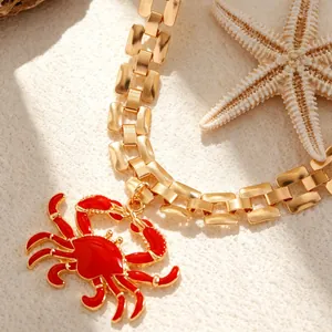 Close-up of red enamel crab pendant on a gold chain necklace for beach vacation style.