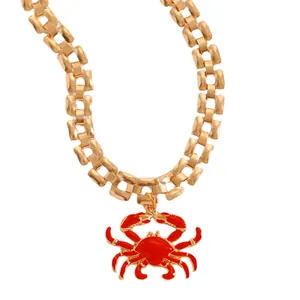 Macro detail view of a chunky gold chain necklace featuring a bright red crab pendant.