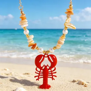 Close-up detail of a red lobster pendant necklace featuring bohemian crushed stones on beach sand