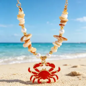 Detail view of red crab pendant necklace with shells and pearls on a sunny beach