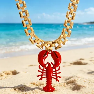 Close-up of a vibrant red lobster pendant on a gold chain against a beach backdrop.