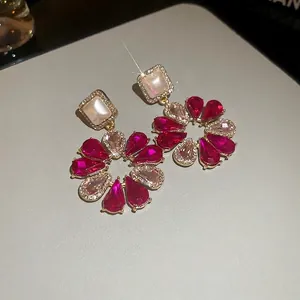 Gros plan de boucles d'oreilles de luxe en cristal fuchsia avec détails dorés et pierres blanches.