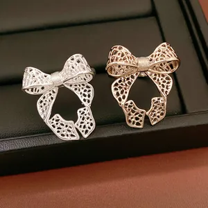 A high-quality close-up detail shot of two exquisite hollow bow-knot open rings in silver and gold colors.