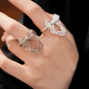 Detail view of two elegant hollow bow rings in gold and silver on a finger.