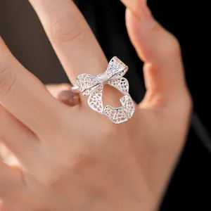Detail view of an elegant silver bow-shaped filigree open ring on a woman's finger.
