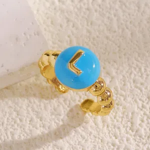 Dettaglio di un anello aperto placcato oro con smalto blu e la lettera L centrale