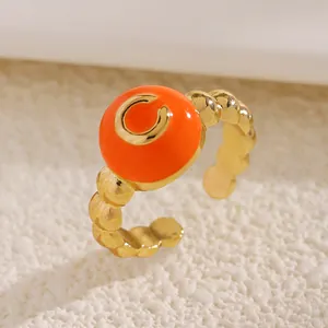 Dettaglio anello regolabile dorato con perline, top in smalto arancione e lettera C