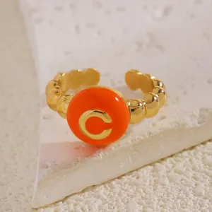 Dettaglio dell'anello aperto a sfere dorate con iniziale C in smalto arancione.