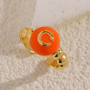 Dettaglio anello aperto a sfere dorate con inserto arancione e lettera C in oro