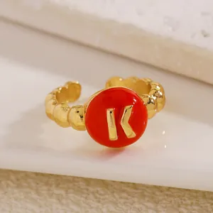 Primo piano di un anello regolabile dorato con dettaglio in smalto rosso e lettera K.