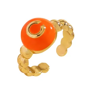 Primo piano di un anello a bolle dorato con smalto arancione e dettaglio della lettera C