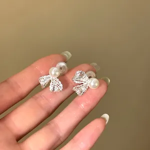Close-up detail view of elegant 18K gold plated pearl bow stud earrings held on fingers