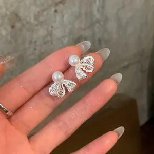 Macro detail of delicate silver mesh bow earrings with centered white pearls.