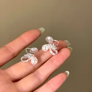 Detailed view of 18K gold plated bow pearl clip-on earrings held on fingertips