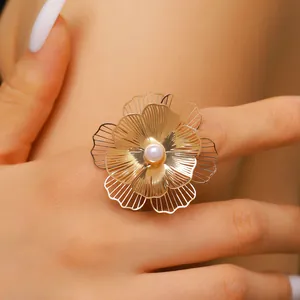 Close-up detail of an oversized gold flower ring with a pearl center worn on a finger