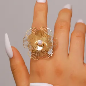 Detailed close-up showing a large gold filigree flower ring with a pearl center worn on a hand