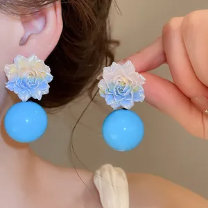 Close-up of blue dopamine resin flower earrings with large round beads worn on ear