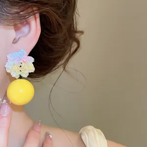 Close-up detail of vibrant resin flower earrings featuring a glossy yellow spherical drop.
