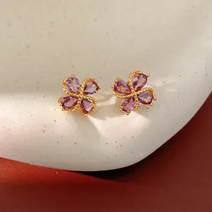 Primer plano de elegantes pendientes de trébol chapados en oro con circonitas moradas en gota