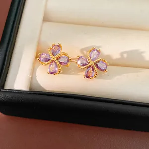 Detalle de elegantes pendientes de trébol en oro de 18k con circonitas púrpuras.