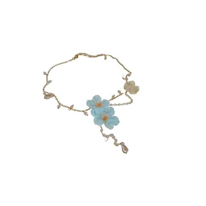 Elegant handmade necklace with blue fabric flowers, pearls, and crystals on a gold chain.