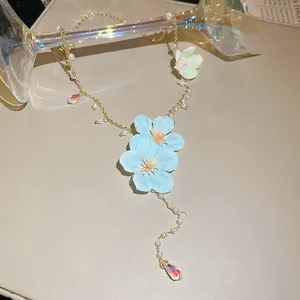 Detailed macro view of light blue cloth flowers and pearls on a gold-tone necklace.
