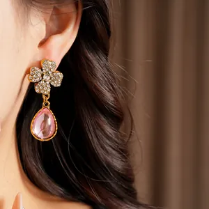 Macro shot of a vintage gold flower earring with a pink resin teardrop on an ear.