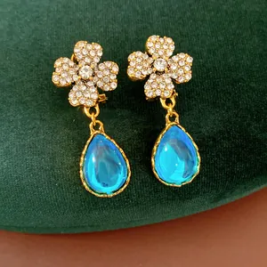 Macro detail of vintage-style gold flower earrings with crystals and blue pear-shaped resin drops