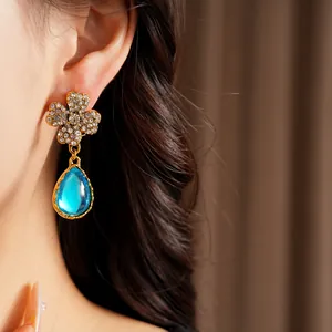 Close-up of vintage gold flower earrings with blue teardrop resin pendant on model