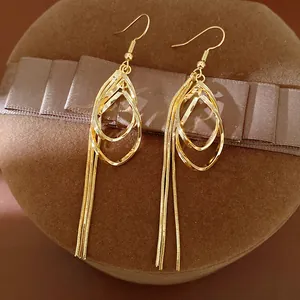 Close-up detail of golden teardrop hollow earrings with long snake chain tassels