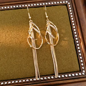 Macro detail showing gold geometric teardrop earrings with elegant long snake chain tassels.