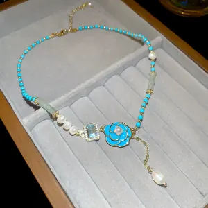Macro detail of blue enamel flower pendant on a dainty freshwater pearl and bead necklace.
