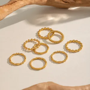 Detailed macro shot of a 7-piece 18K gold plated bamboo and twisted ring set on sand texture