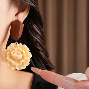A detailed close-up of ethnic style earrings featuring a wood top and resin flower.