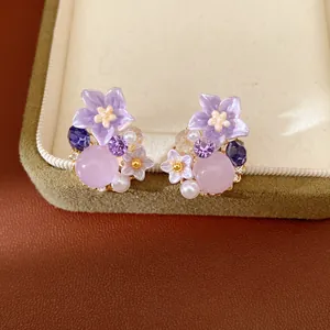 Dettaglio di orecchini a lobo a fiore in resina viola con perle e zirconi