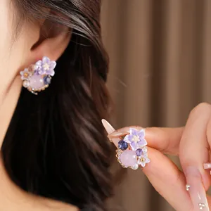 Dettaglio di orecchini a fiore in resina viola con aghi d'argento e perline rosa.
