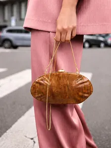 Detail of amber marble acrylic shell clutch with gold metal chain on pink outfit