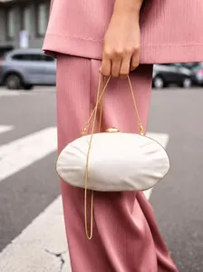 Detail of white satin shell evening bag with gold metal frame and ball clasp held by model