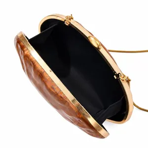Macro view of shell-shaped acrylic clutch with amber pattern and gold chain strap